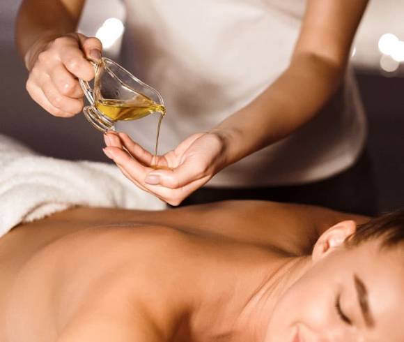 Therapeutin hält wohltuendes Massageöl über dem Rücken für eine entspannende Thai-Ölmassage.