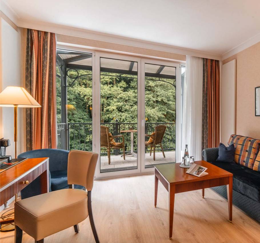 Granitz Deluxe Room at the Grand Hotel Binz with large windows, sofa, table, and balcony with a view of the countryside.