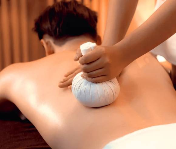 Anwendung einer lösenden Kräuterstempelmassage am Rücken eines Mannes.