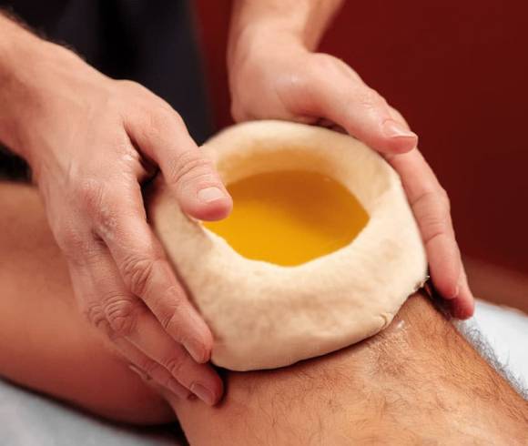 Ayurveda-Teigring an einem Knie, gefüllt mit beruhigendem Kräuteröl.