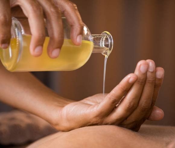 Massage therapist prepares oil massage – a gentle start to a wellness treatment with a wide range of fragrances.
