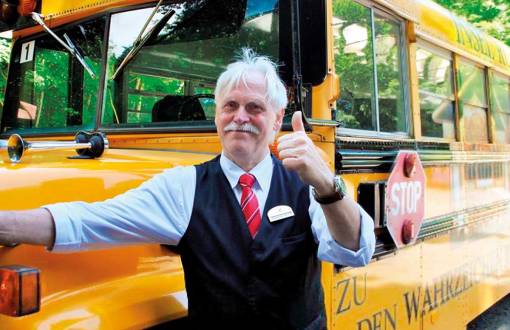 Ein freundlicher Fahrer vor einem nostalgischen Schulbus vorm Grand Hotel Binz, bereit zur Abfahrt zum Kap Arkona.