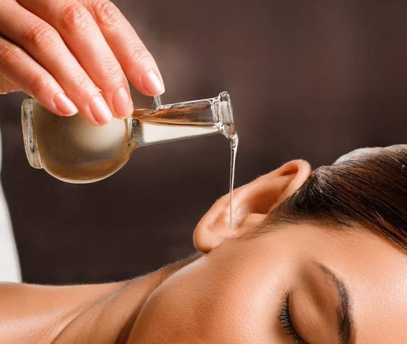 Kräuteröl fließt in das Ohr eines zufrieden lächelnden Spa-Gastes.