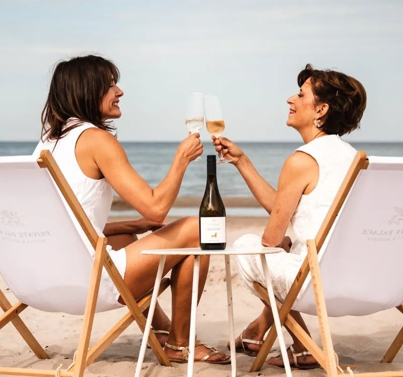 Zwei Frauen stoßen am Strand von Rügen mit Sekt auf ihren gemeinsamen Urlaub an