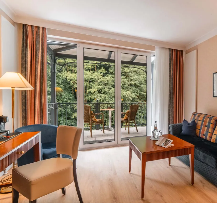 Granitz Deluxe Room at the Grand Hotel Binz with large windows, sofa, table, and balcony with a view of the countryside.