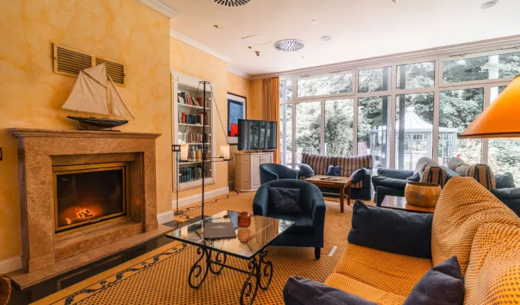 The cozy fireplace lounge of the Grand Hotel Binz with armchairs, a fireplace, and a view of the garden.