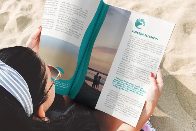 Frau am Strand mit OMWS-Magazin – Grand Hotel Binz beteiligt sich an der Nachhaltigkeitsbewegung „Ohne Meer wird schwer“