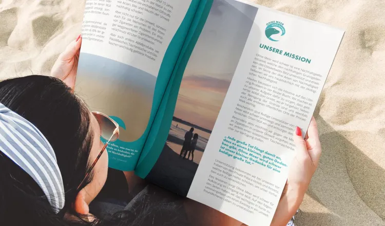 Frau am Strand mit OMWS-Magazin – Grand Hotel Binz beteiligt sich an der Nachhaltigkeitsbewegung „Ohne Meer wird schwer“