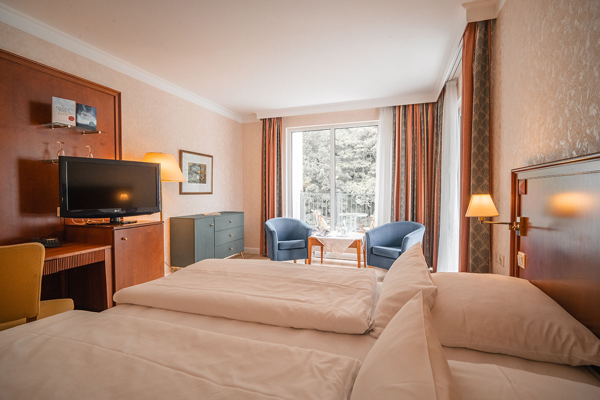 Large double bed, sitting area with access to the roof terrace, and desk with TV at the Grand Hotel Binz.