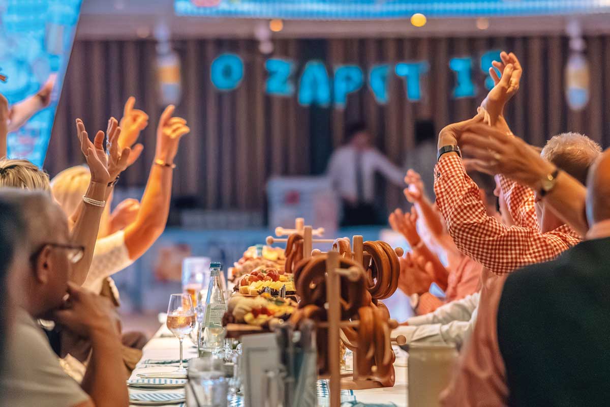 Gäste feiern mit erhobenen Armen beim 4. Binzer Oktoberfest mit Bier, Wein, Brezeln und festlichen Dekorationen im Arkona Strandhotel.
